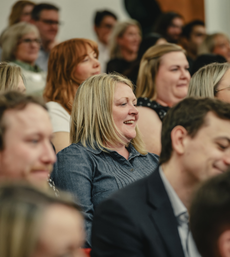 A woman smiling in the audience at a conference 